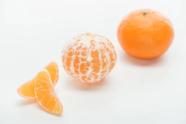 Foco selectivo de mandarinas maduras de color naranja entero peladas y sin pelar con rodajas sobre fondo blanco - foto de stock