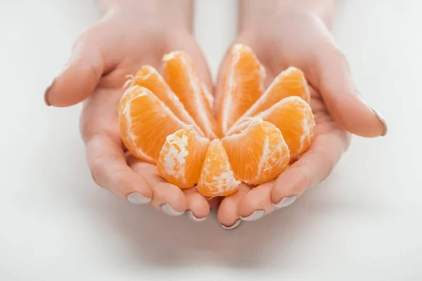 Vista recortada de la mujer sosteniendo rodajas de mandarina naranja madura dispuestas en círculo sobre fondo blanco - foto de stock
