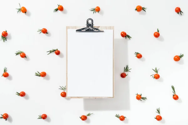 Vue du dessus du presse-papiers vierge avec tomates cerises et feuilles sur fond blanc — Photo de stock