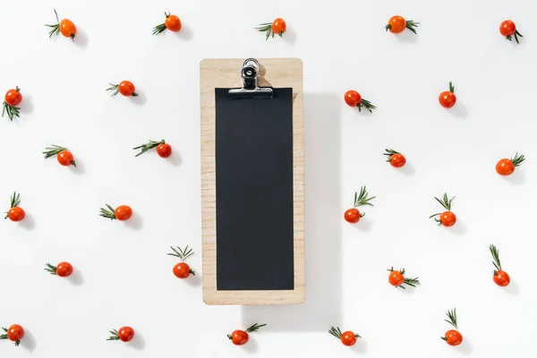 Top view of empty clipboard with cherry tomatoes and leaves on white background — Stock Photo