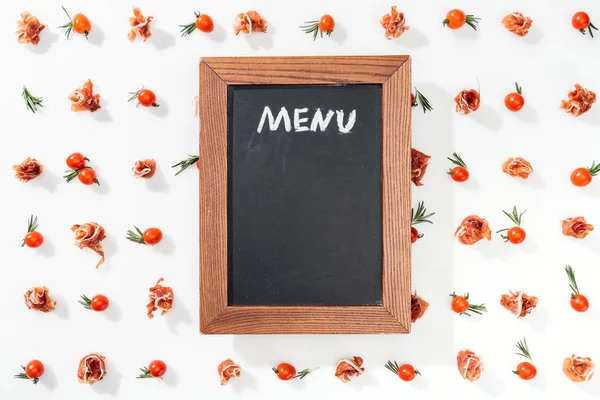Pizarra con letras de menú entre tomates cherry, prosciutto y hojas - foto de stock