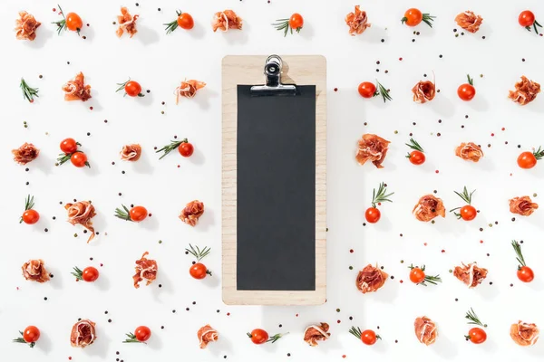 Top view of blank clipboard with cherry tomatoes, leaves, spices and prosciutto — Stock Photo