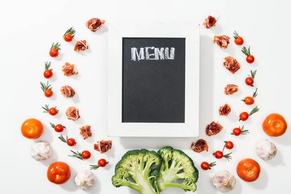 Chalk board with menu lettering among tomatoes, prosciutto, broccoli, onion and garlic — Stock Photo