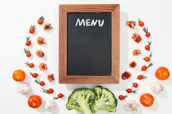 Top view of black chalk board with menu lettering among tomatoes, prosciutto, broccoli and garlic — Stock Photo