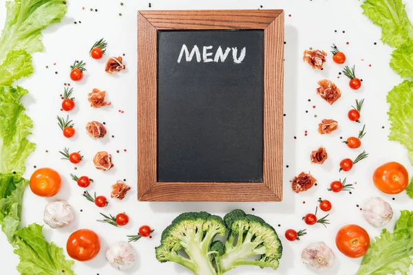 Vista superior de pizarra con letras de menú entre tomates, hojas de lechuga, jamón, brócoli, especias y ajo - foto de stock