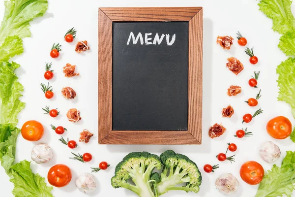 Top view of chalk board with menu lettering among tomatoes, lettuce leaves, prosciutto, broccoli and garlic — Stock Photo