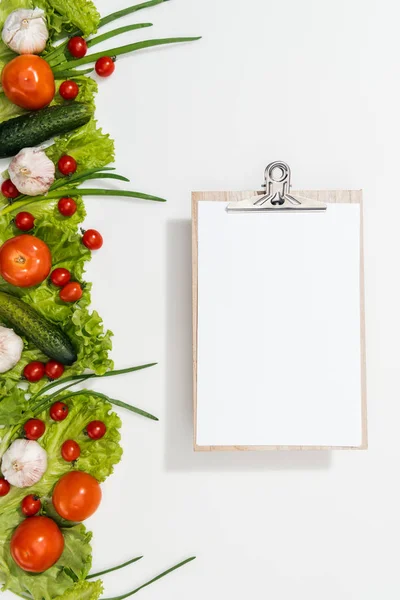 Top view of clipboard with tomatoes, lettuce leaves, cucumbers, onion and garlic — Stock Photo