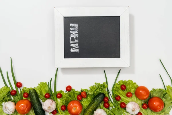 Vue du dessus de la planche à craie avec lettrage de menu parmi les tomates, feuilles de laitue, concombres, oignon et ail — Photo de stock