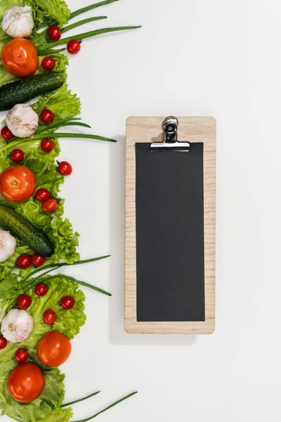 Top view of empty clipboard with tomatoes, lettuce leaves, cucumbers, onion and garlic — Stock Photo