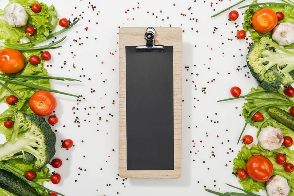 Top view of empty clipboard with tomatoes, lettuce leaves, cucumbers, onion, spices and garlic — Stock Photo