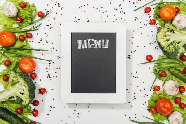 Kreidetafel mit Menüaufdruck zwischen Tomaten, Salatblättern, Gurken, Zwiebeln, Gewürzen und Knoblauch — Stockfoto