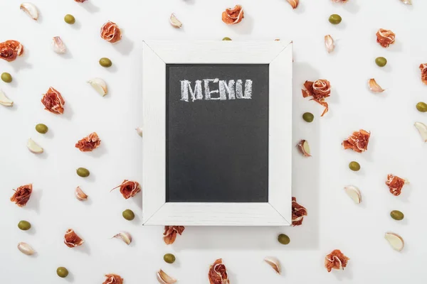 Vista dall'alto del pannello di gesso con scritte di menu tra prosciutto, olive e spicchi d'aglio — Foto stock