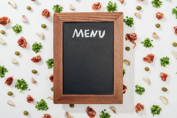 Top view of chalk board with menu lettering among prosciutto, olives, garlic cloves and greenery — Stock Photo