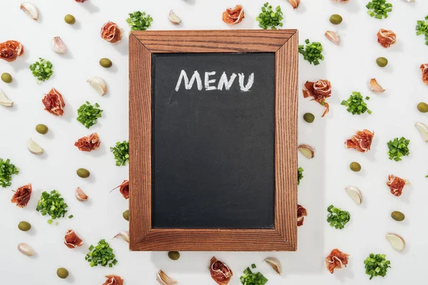 Vista superior de tábua de giz com letras de menu entre presunto, azeitonas, dentes de alho e vegetação — Fotografia de Stock