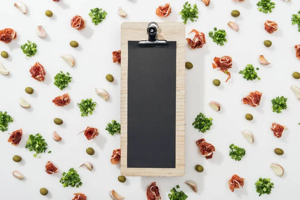 Top view of empty clipboard among prosciutto, olives, garlic cloves and greenery — Stock Photo