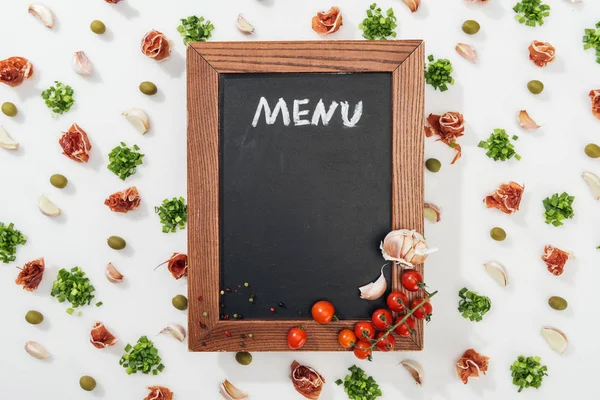 Vista superior de pizarra con letras de menú entre prosciutto, aceitunas, dientes de ajo, vegetación y tomates cherry - foto de stock