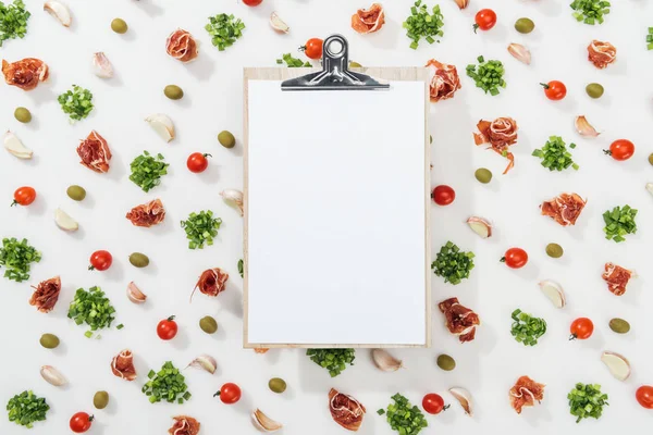 Top view of empty clipboard among prosciutto, olives, garlic cloves, greenery and cherry tomatoes — Stock Photo