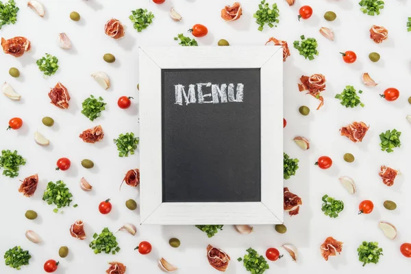 Top view of chalk board with menu lettering among prosciutto, olives, garlic cloves, greenery and cherry tomatoes — Stock Photo