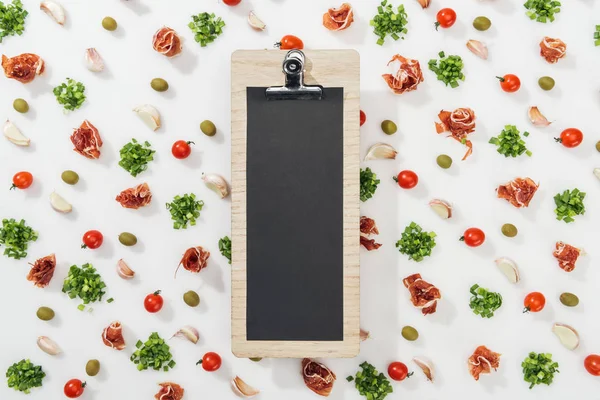 Empty clipboard among prosciutto, olives, garlic cloves, greenery and cherry tomatoes — Stock Photo