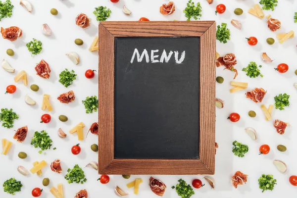 Chalk board with menu lettering among olives, garlic cloves, prosciutto, greenery, cut cheese and cherry tomatoes — Stock Photo