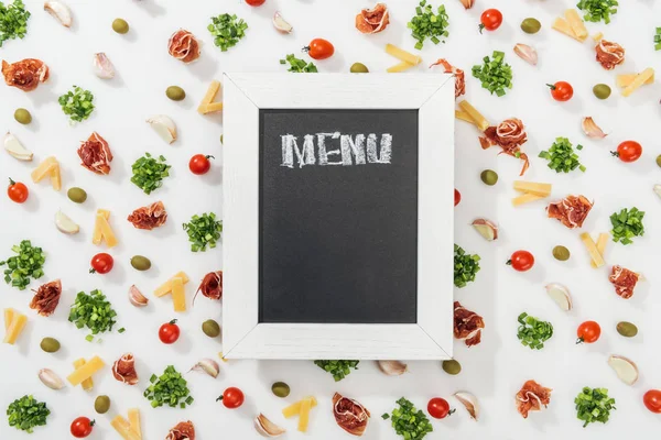 Top view of chalk board with menu lettering among olives, prosciutto, greenery, cut cheese, garlic cloves and cherry tomatoes — Stock Photo