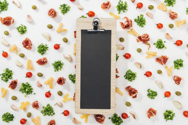 Clipboard among olives, prosciutto, greenery, cut cheese, garlic cloves and cherry tomatoes — Stock Photo