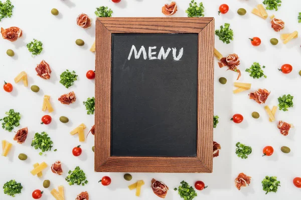 Vista superior de pizarra con letras de menú entre aceitunas, jamón, verdor, queso cortado y tomates cherry - foto de stock