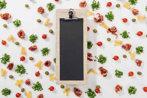 Top view of clipboard among olives, prosciutto, greenery, cut cheese and cherry tomatoes — Stock Photo