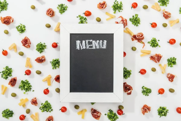 Chalk board with menu lettering among olives, prosciutto, greenery, cut cheese and cherry tomatoes — Stock Photo