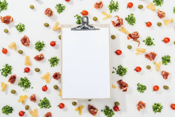 White clipboard among olives, prosciutto, greenery, cut cheese and cherry tomatoes — Stock Photo