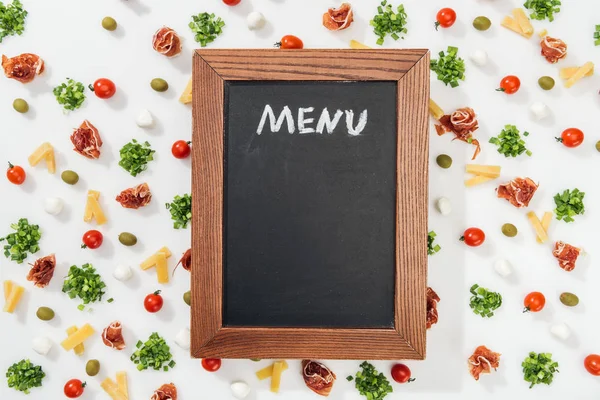 Chalk board with menu lettering among olives, prosciutto, greenery, mozzarella, cut cheese and cherry tomatoes — Stock Photo