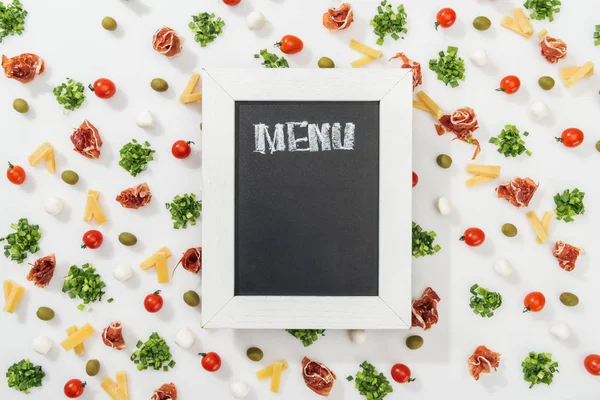 Chalk board with menu lettering among olives, prosciutto, greenery, mozzarella, cut cheese and cherry tomatoes — Stock Photo