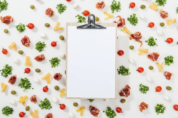 Empty clipboard with menu lettering among olives, prosciutto, greenery, mozzarella, cut cheese and cherry tomatoes — Stock Photo