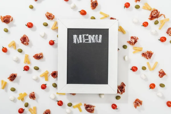 Chalk board with menu lettering among olives, prosciutto, mozzarella, cut cheese and cherry tomatoes — Stock Photo