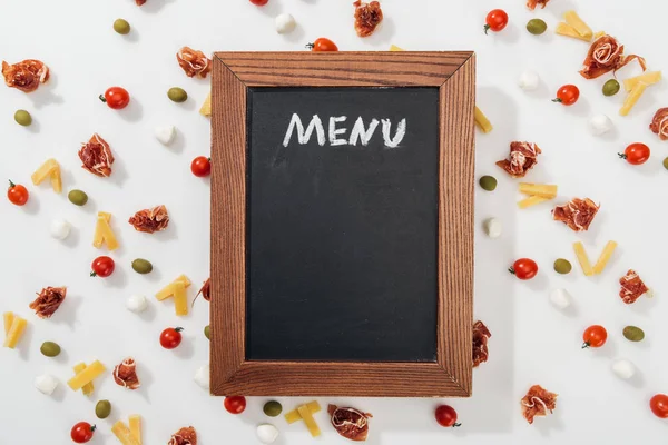 Chalk board with menu lettering among olives, prosciutto, mozzarella, cut cheese and cherry tomatoes — Stock Photo