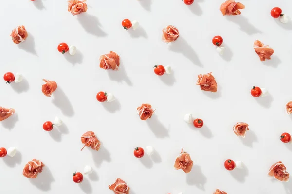 Top view of raw prosciutto near red cherry tomatoes on white background — Stock Photo