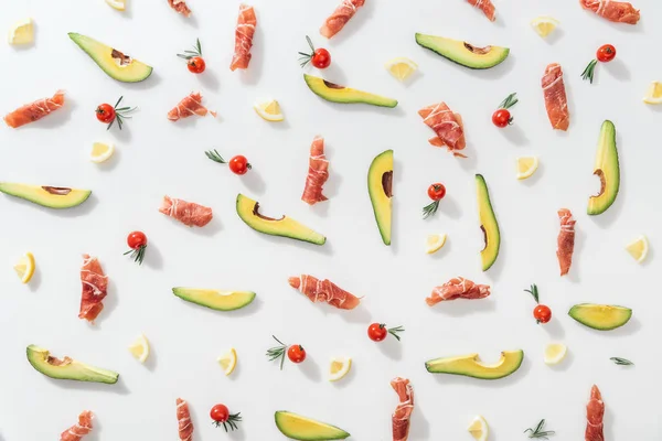 Draufsicht auf schmackhaften Prosciutto in der Nähe von roten Kirschtomaten, Avocados und Zitronen auf weißem Hintergrund — Stockfoto