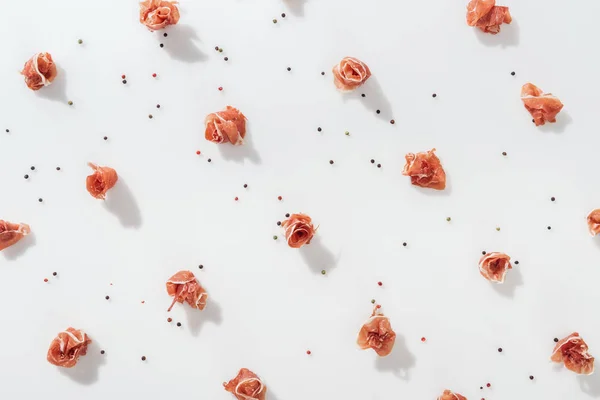 Vue de dessus de savoureux prosciutto près de grains de poivre noirs et rouges sur fond blanc — Stock Photo