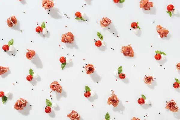 Вид зверху смачного прошутто поблизу червоних вишневих помідорів, сиру моцарелла та перцю на білому тлі — стокове фото