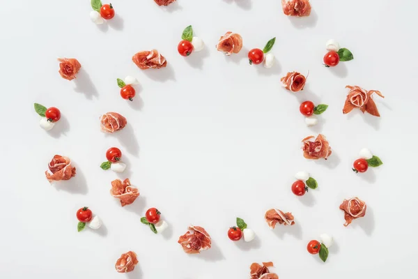 Plat de savoureux prosciutto près de tomates cerises rouges, fromage mozzarella et feuilles de basilic vert sur fond blanc — Photo de stock