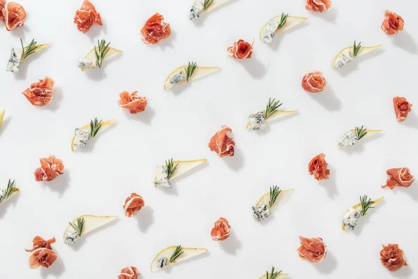 Flat lay of prosciutto near sliced pears with blue cheese and rosemary twigs on white background — Stock Photo