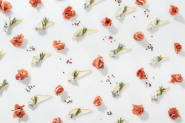 Flat lay of delicious prosciutto near sliced pears with blue cheese and rosemary twigs on white background — Stock Photo