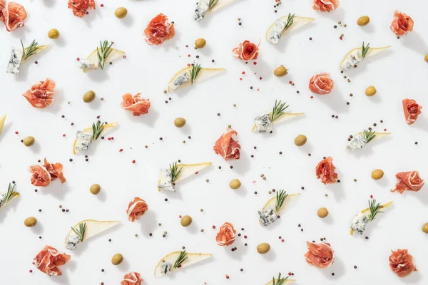 Flat lay of sliced pears with blue cheese and rosemary twigs near green olives and tasty prosciutto on white background — Stock Photo