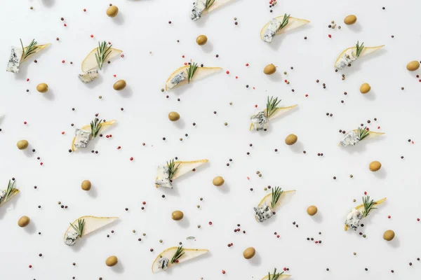 Vue de dessus des poires tranchées avec du fromage bleu et des brindilles de romarin près des grains de poivre et des olives vertes sur fond blanc — Photo de stock