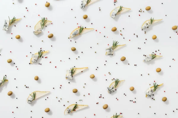 Top view of sliced pears with blue cheese and rosemary twigs near peppercorns and green olives on white background — Stock Photo