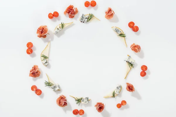 Vue de dessus de poires tranchées au fromage bleu et brindilles de romarin près de savoureux prosciutto et tomates cerises sur fond blanc — Photo de stock