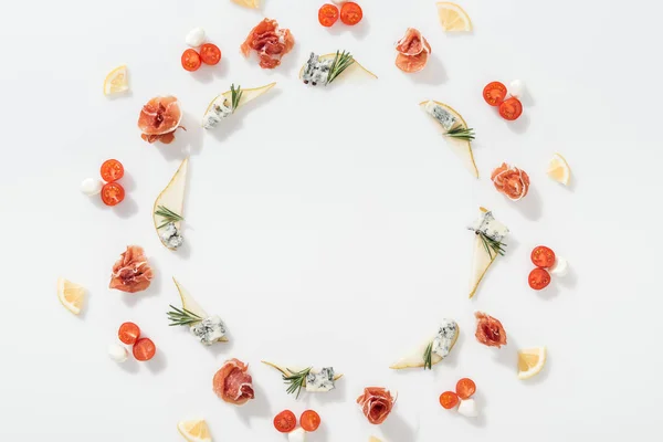 Top view of sliced pears with blue cheese and rosemary twigs near prosciutto, cherry tomatoes and mozzarella cheese on white background — Stock Photo