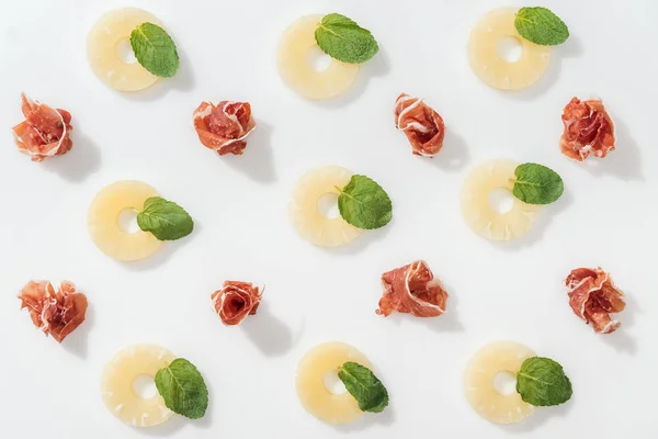 Top view of delicious prosciutto near green basil leaves and pineapple rings on white background — Stock Photo