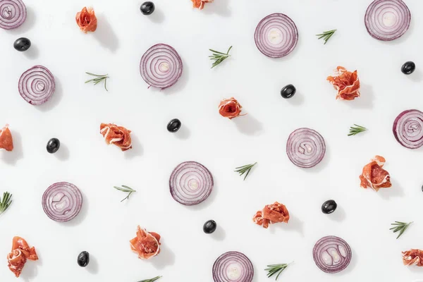 Flat lay of red onion rings near prosciutto, cherry tomatoes, rosemary twigs and black olives on white background — Stock Photo