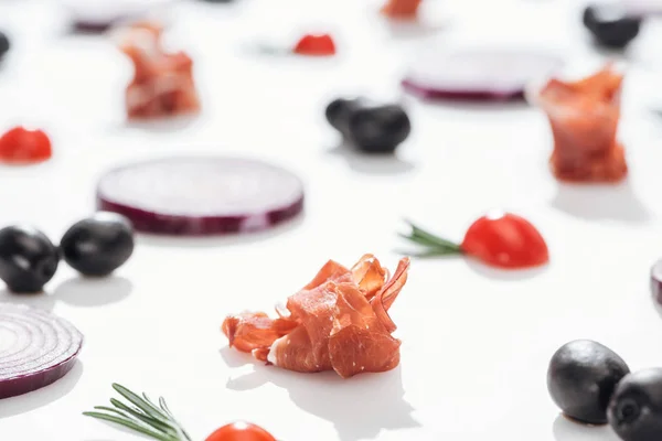 Enfoque selectivo de delicioso prosciutto cerca de tomates cherry con ramitas de romero y anillos de cebolla roja sobre fondo blanco - foto de stock
